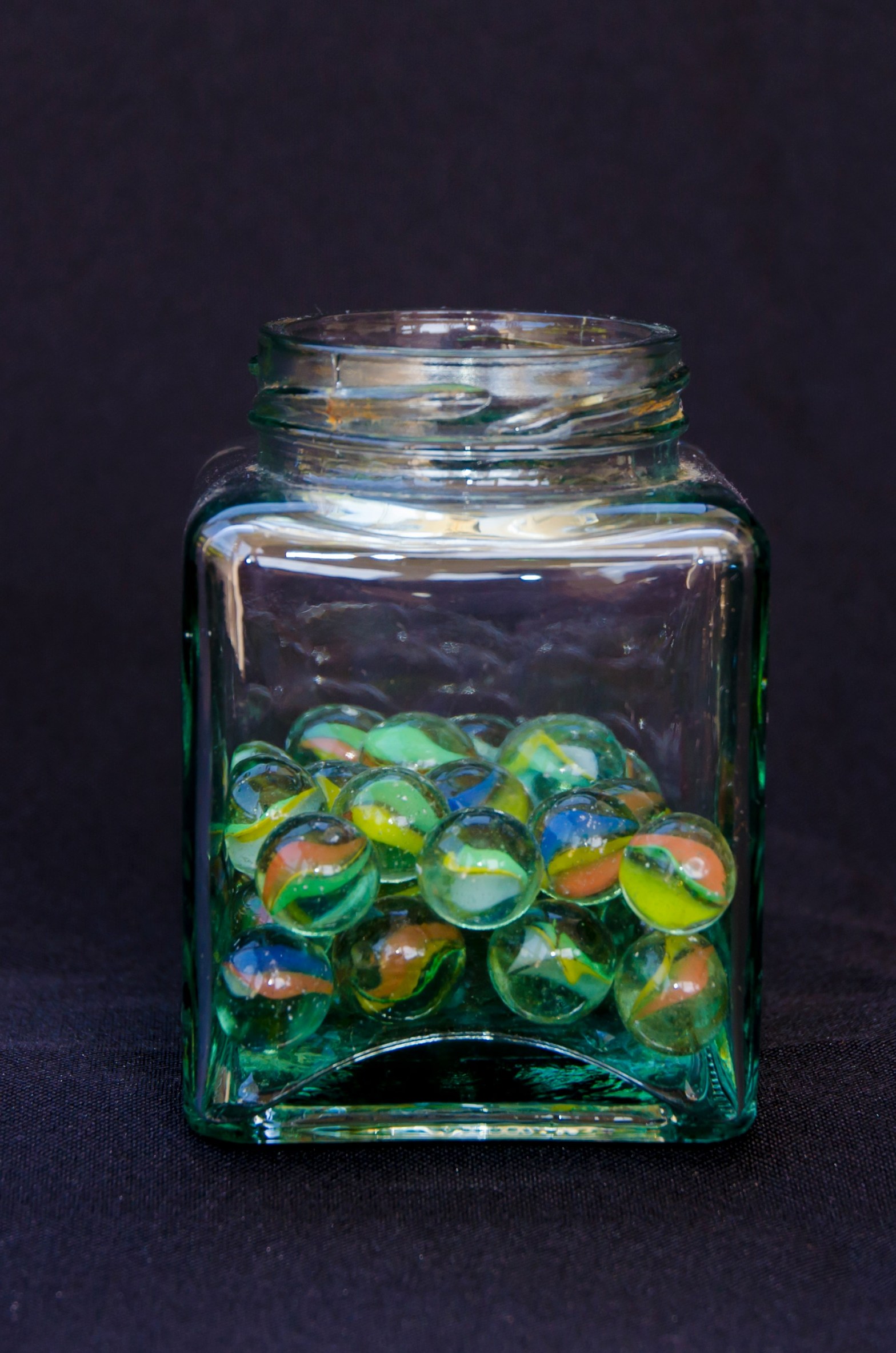 Glass jar half full of multiple colors of marbles